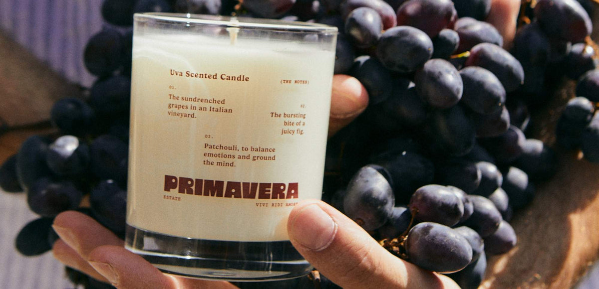 Hand holding the Earl of East Uva scented candle in front of a bunch of red grapes